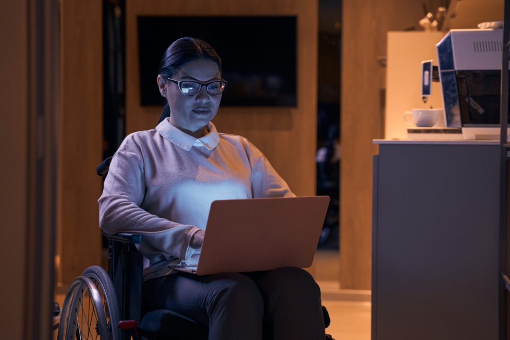Frau im Rollstuhl sitzt mit Laptop im Schoß